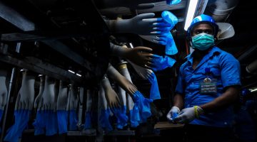 An employee monitors latex gloves on hand-shaped molds moving along an automated production line at a Top Glove Corp. factory in Malaysia