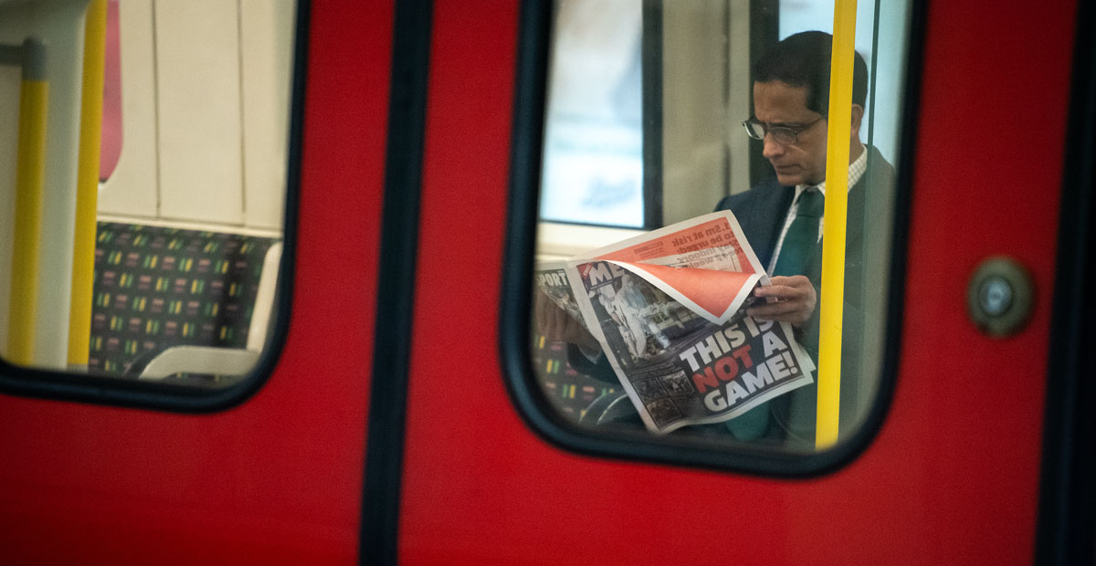 a man reading a newspaper covering the coronavirus on the london train.