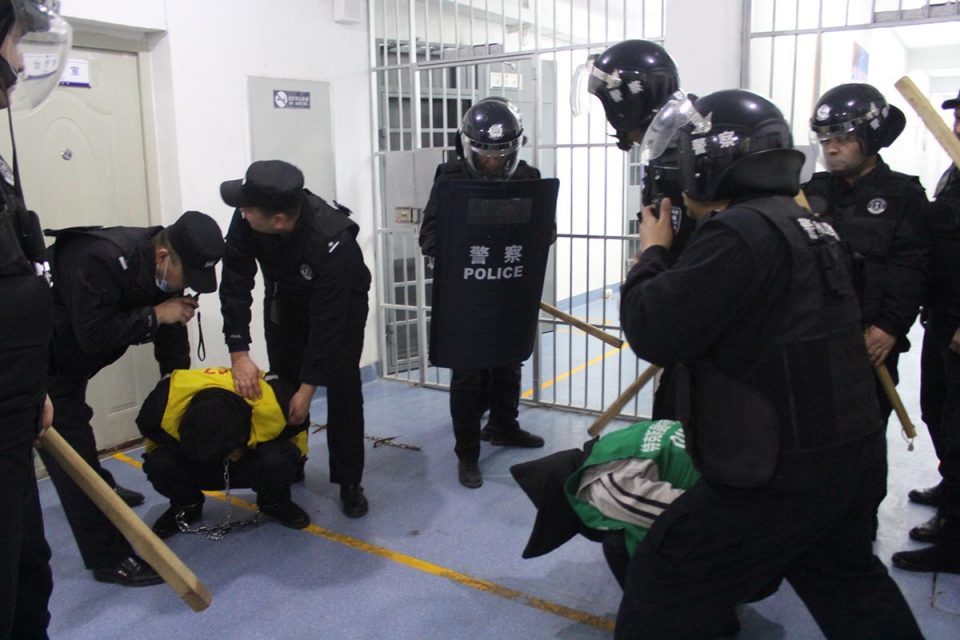 Photo showing guards in riot gear with weapons standing over crouching detainees
