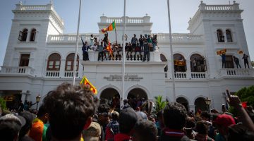 Photo of protesters climbing a building and waving Sri Lankan flags