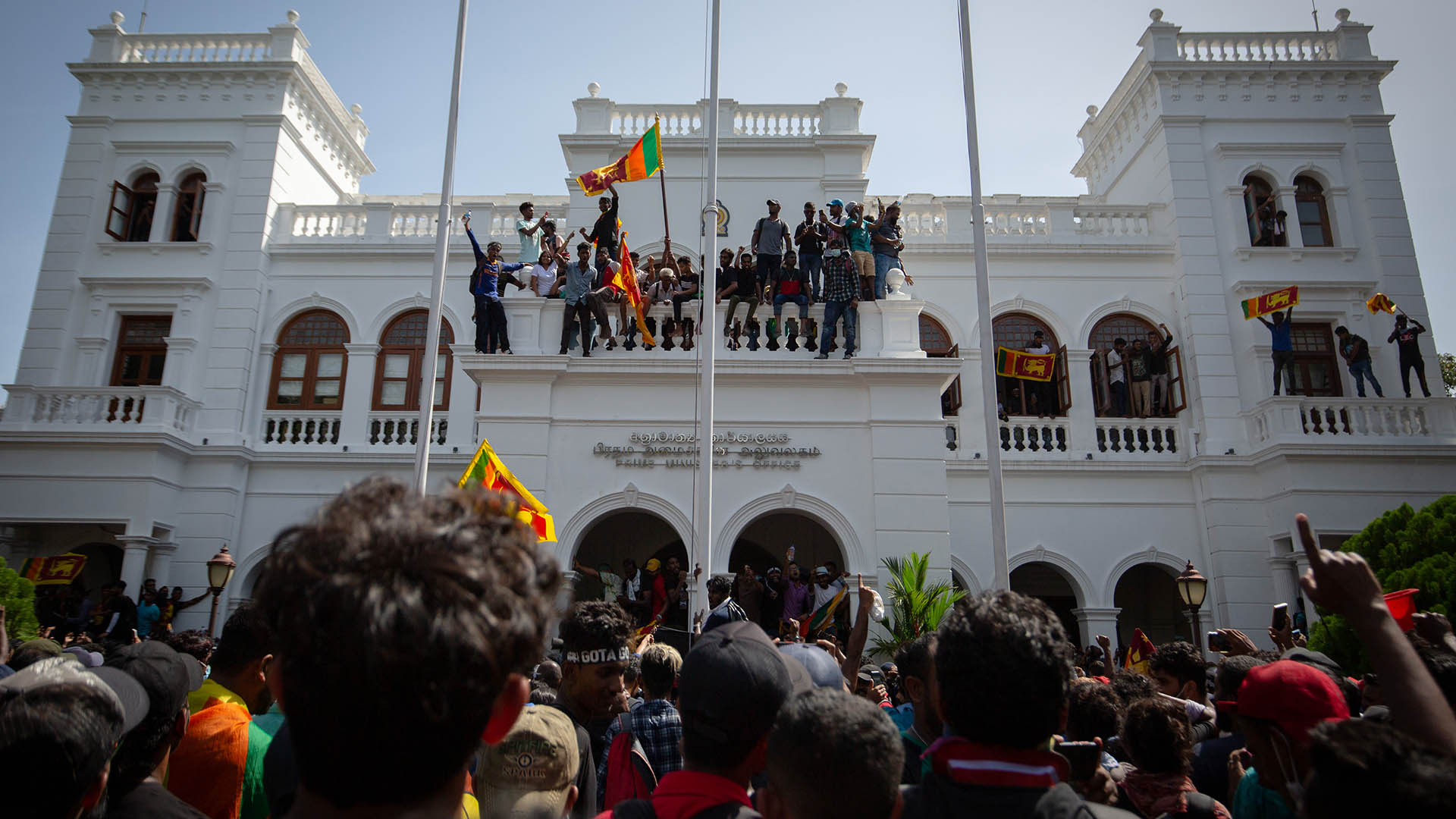 Photo of protesters climbing a building and waving Sri Lankan flags