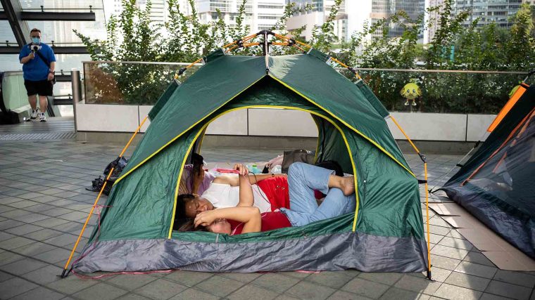 Two people sleep in an pen-air tent at a train station in Hong Kong