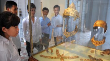 A group of students look at a museum display of ancient Cambodian artifacts
