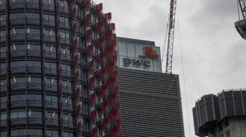 A red and grey office building with a PwC logo on a cloudy day