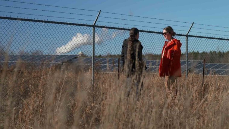 Two women standing in a field in front of a solar panel farm.