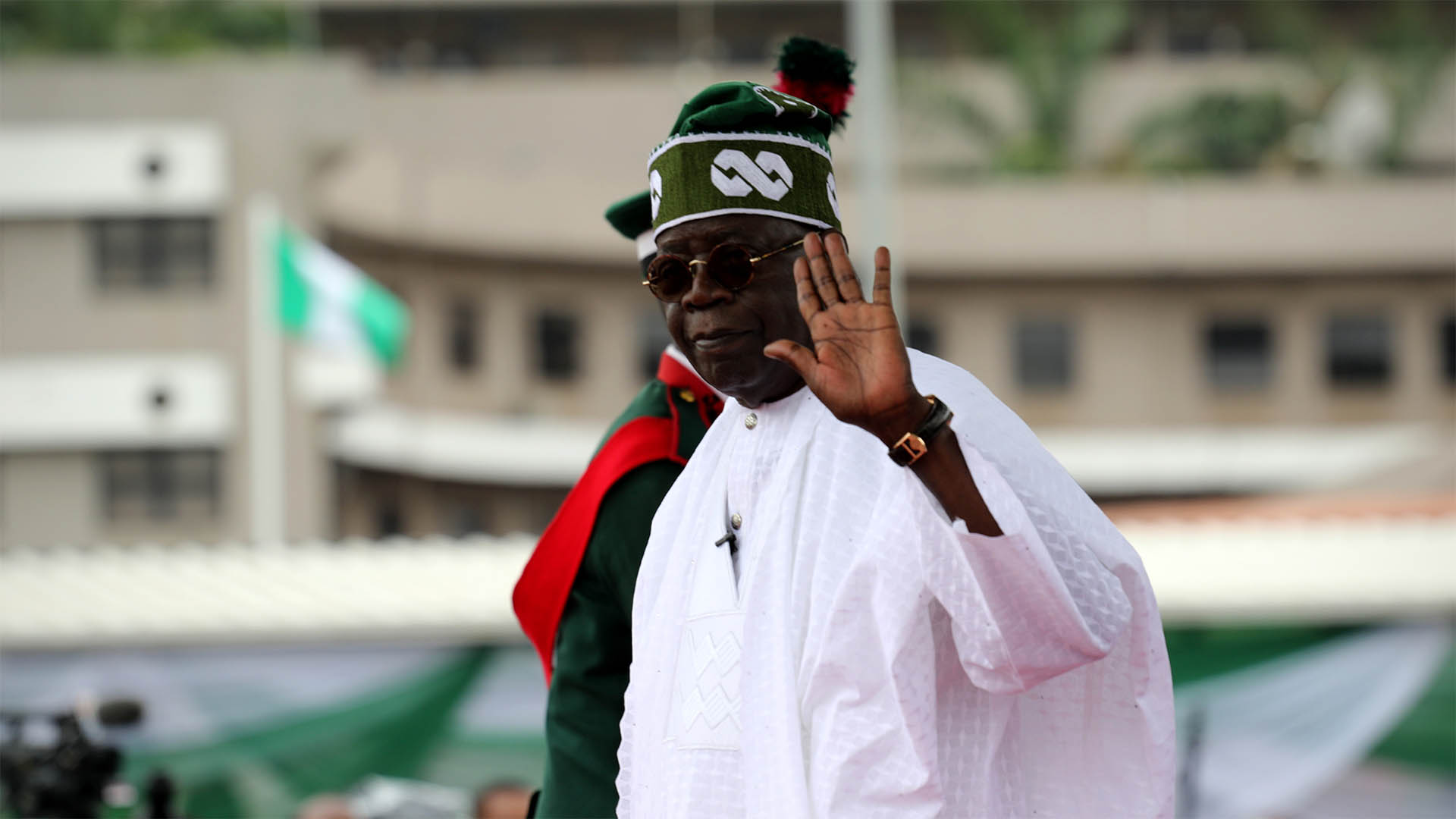 Bola Tinubu in green cap and white robes waving