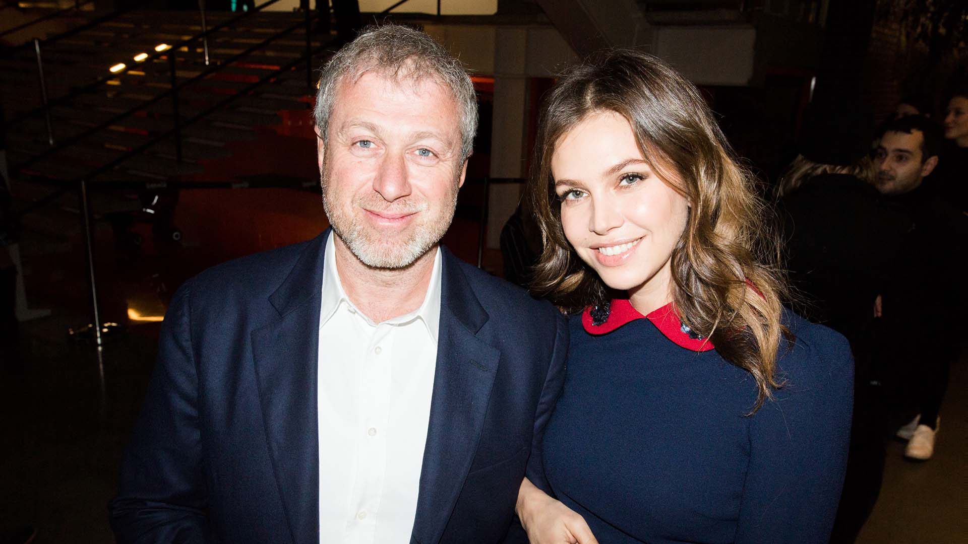 A couple stand together, linking arms andsmiling at a gallery opening