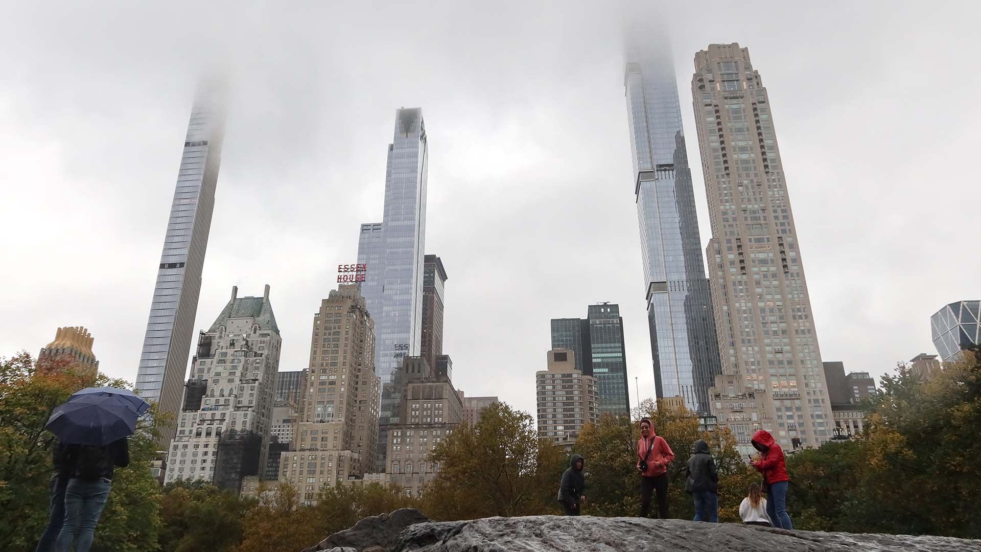 A group of people with umbrellas stand in front of luxury-apartment buildings in New York City.