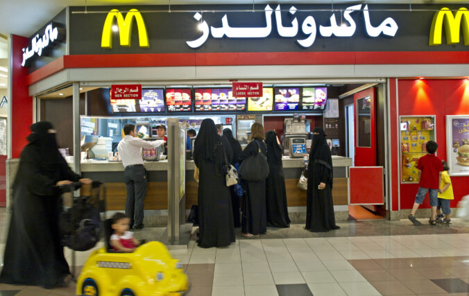 Women in black niqab line up for a McDonald's with the store name written in white Arabic lettering.