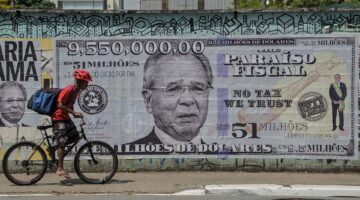 A man rides his bike past a poster depicting Brazil's Economy Minister Paulo Guede.