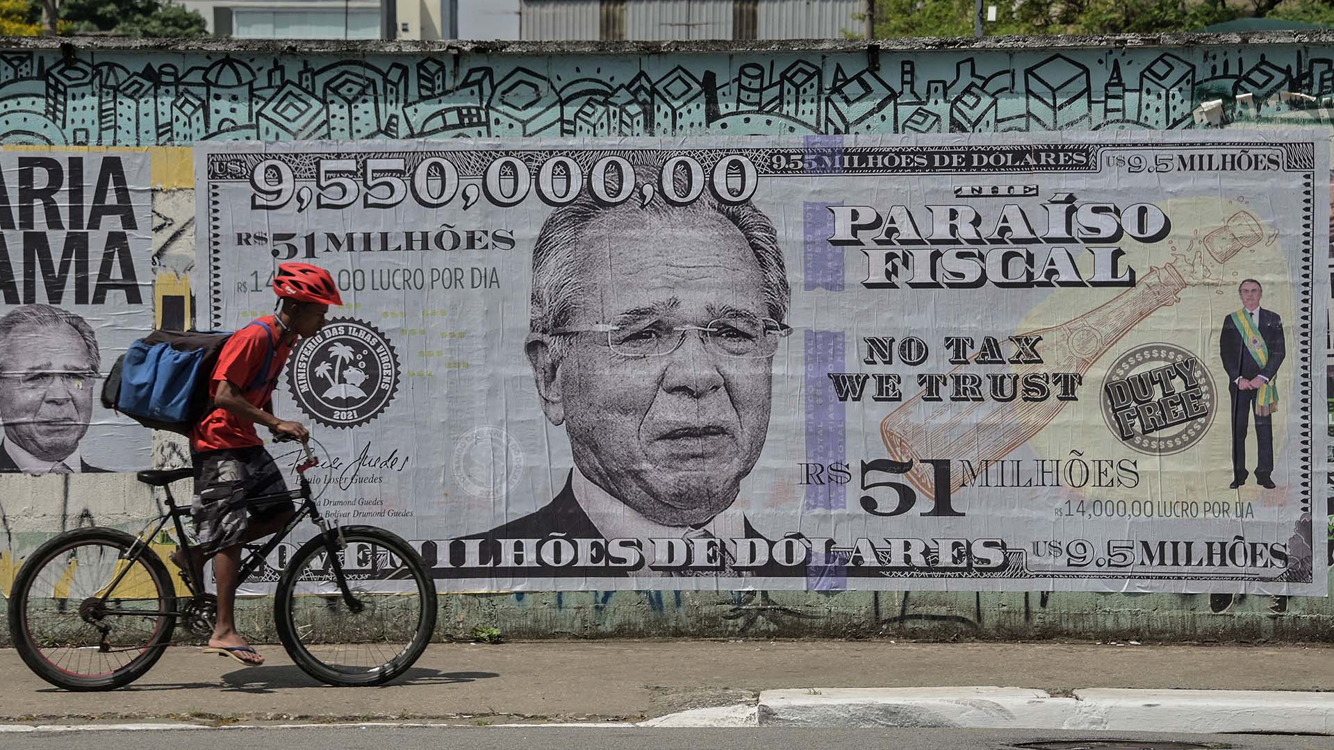 A man rides his bike past a poster depicting Brazil's Economy Minister Paulo Guede.