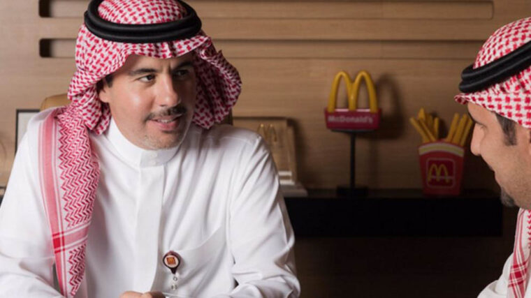 Prince Mishaal Al-Saud speaking with a man to his right, with the Mcdonald's logo featured behind them.
