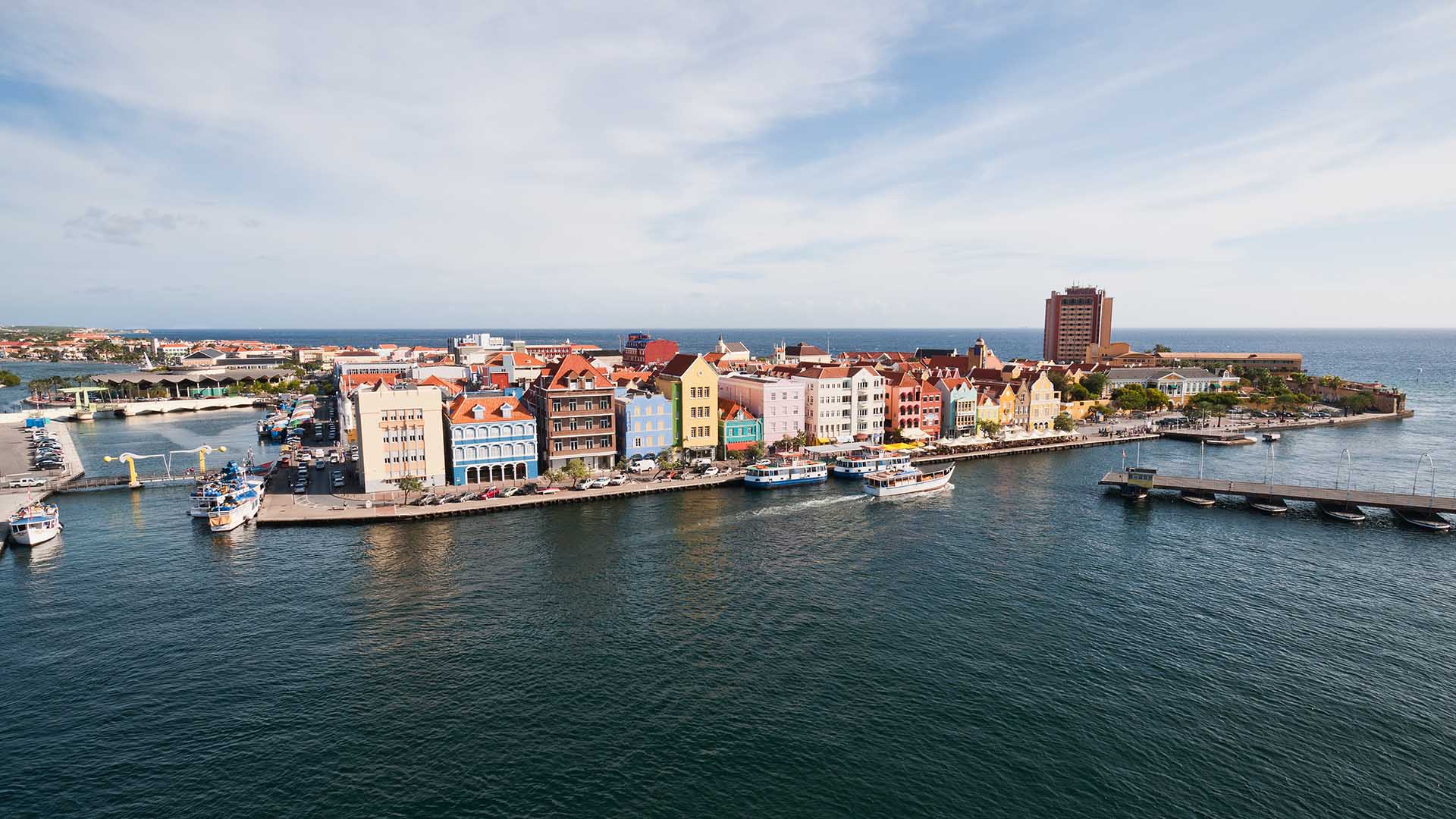 Aerial photo showing colorful, short buildings along the edge of a blue harbor.