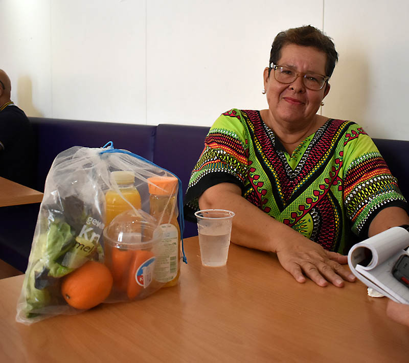 Woman at a cafe table with a bag of groceries on the table.