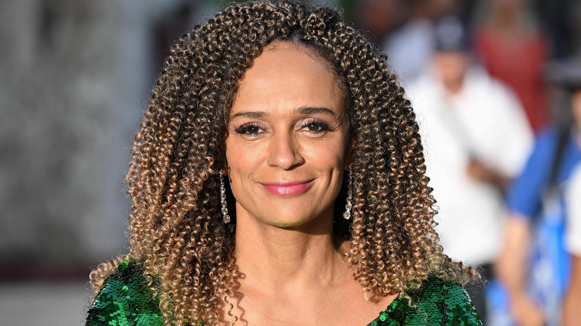 A woman with curly hair and a sequined green dress smiling