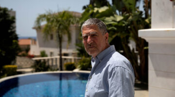 Grey-haired man in blue shirt standing in front of a swimming pool