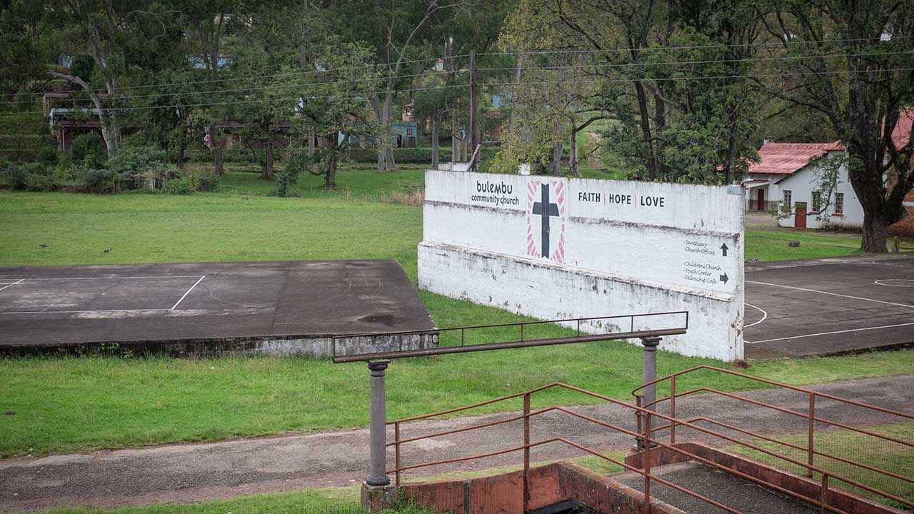 A freestanding white wall in between two concrete sports courts with a painted sign that reads Bulembu Community Church.