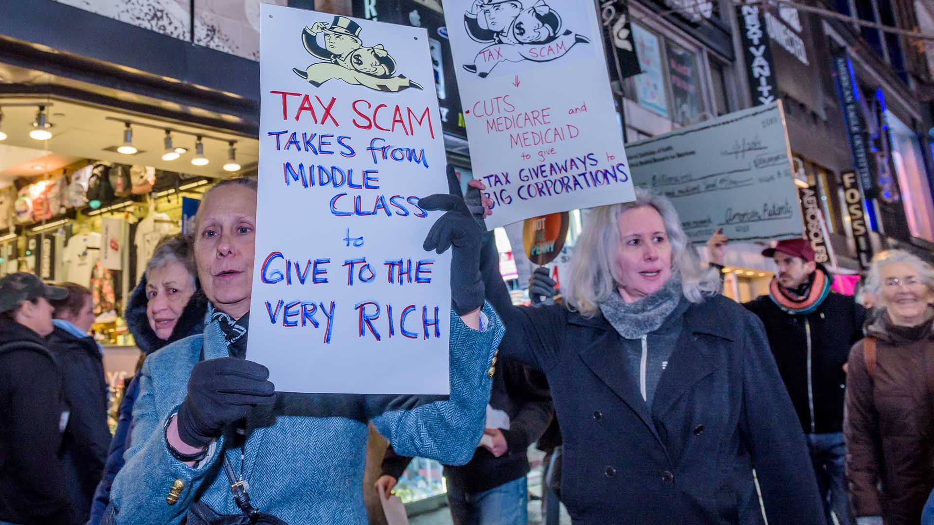Protesters hold up handmade signs with written messages about tax scams and inequality.