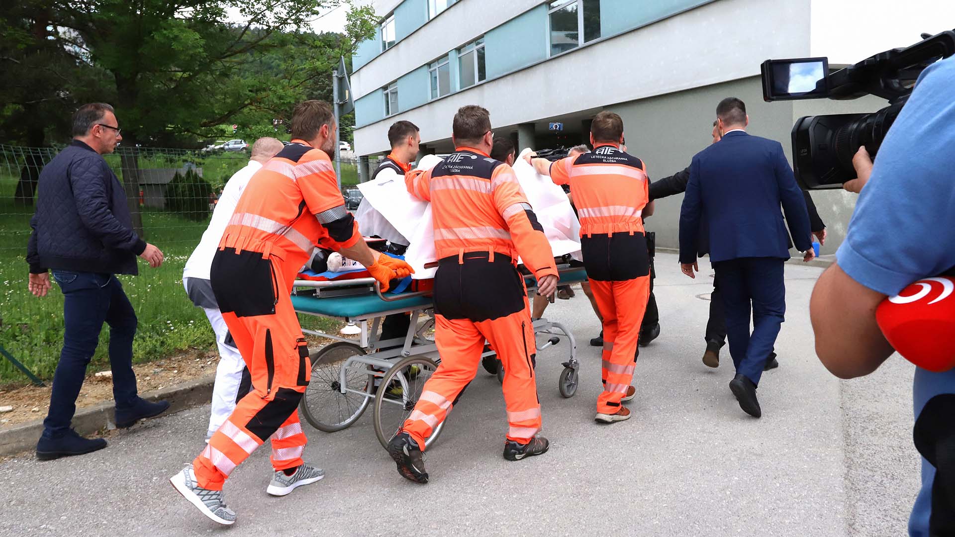 Photo of emergency workers wheeling a bed into a hospital as media and security agents watch on.