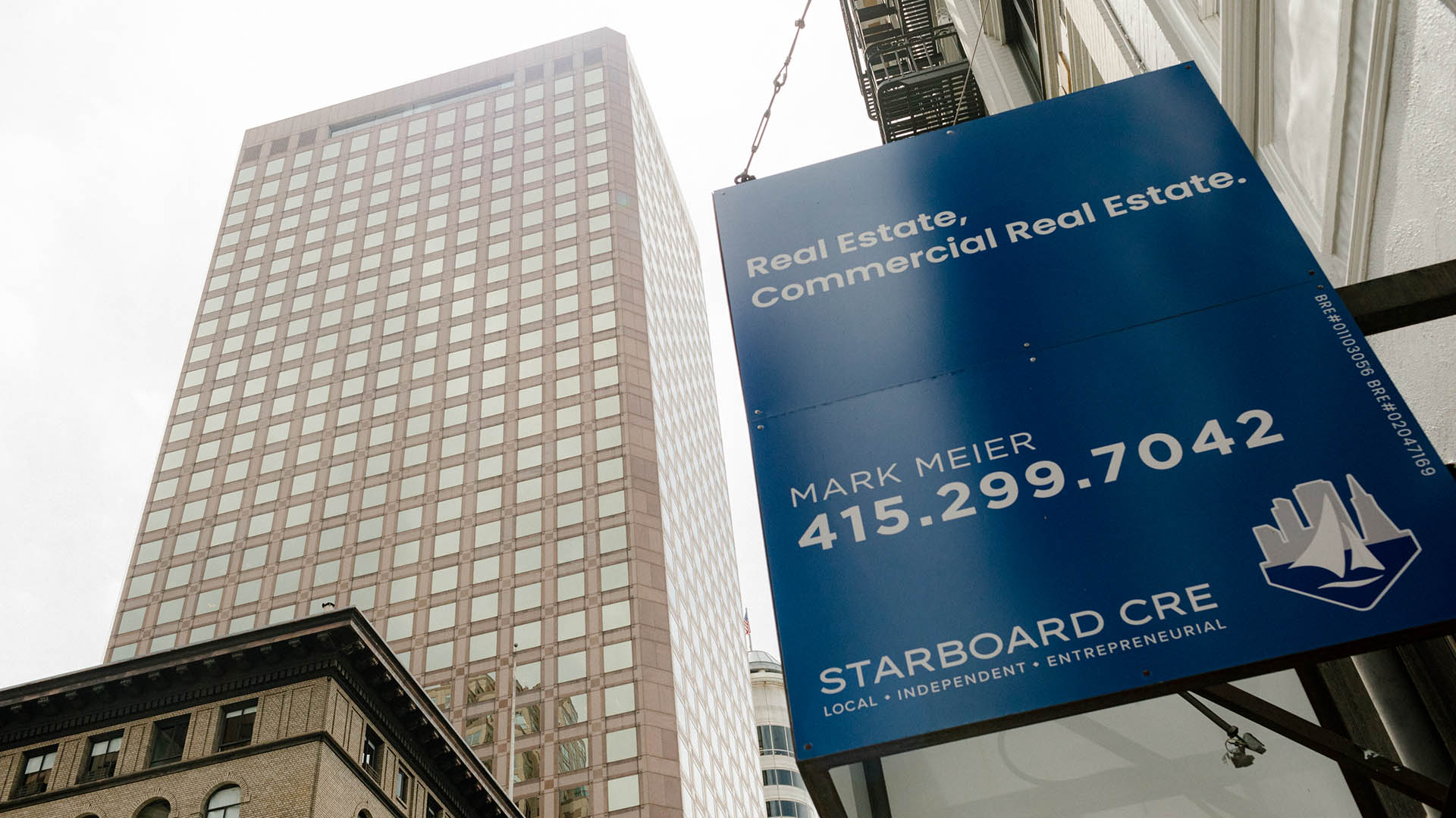 A blue "Commercial Real Estate" sign in front a gray skyscraper