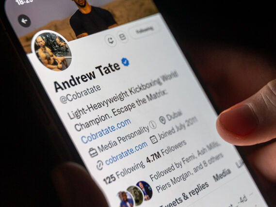 In this photo illustration a man looks at his phone displaying the social media Twitter page for Andrew Tate