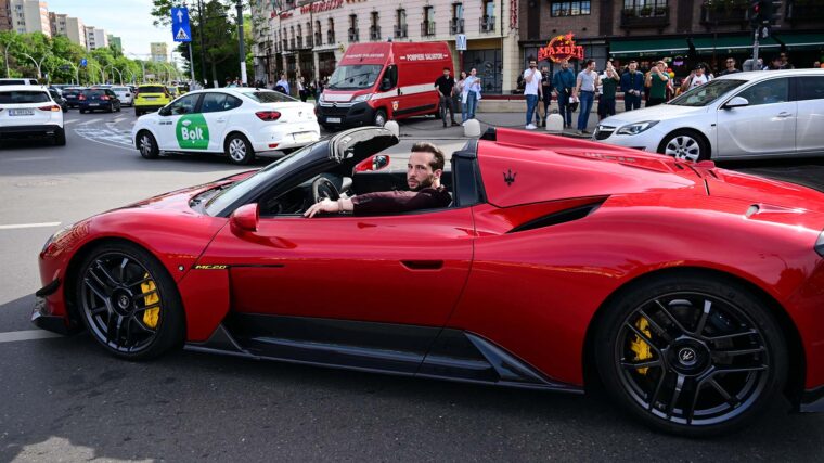 A man with a beard in a red sport car stares at the camera