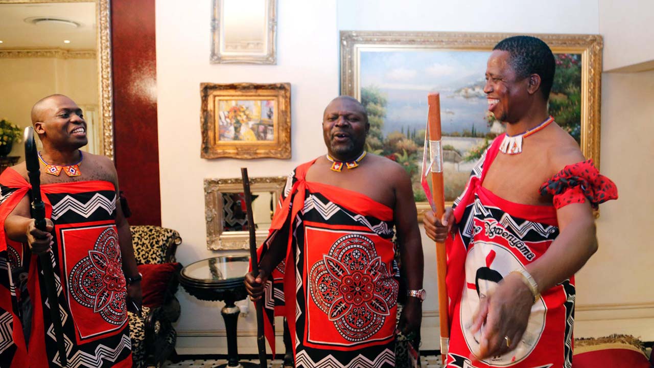 Three men in traditional Swazi dress laughing.