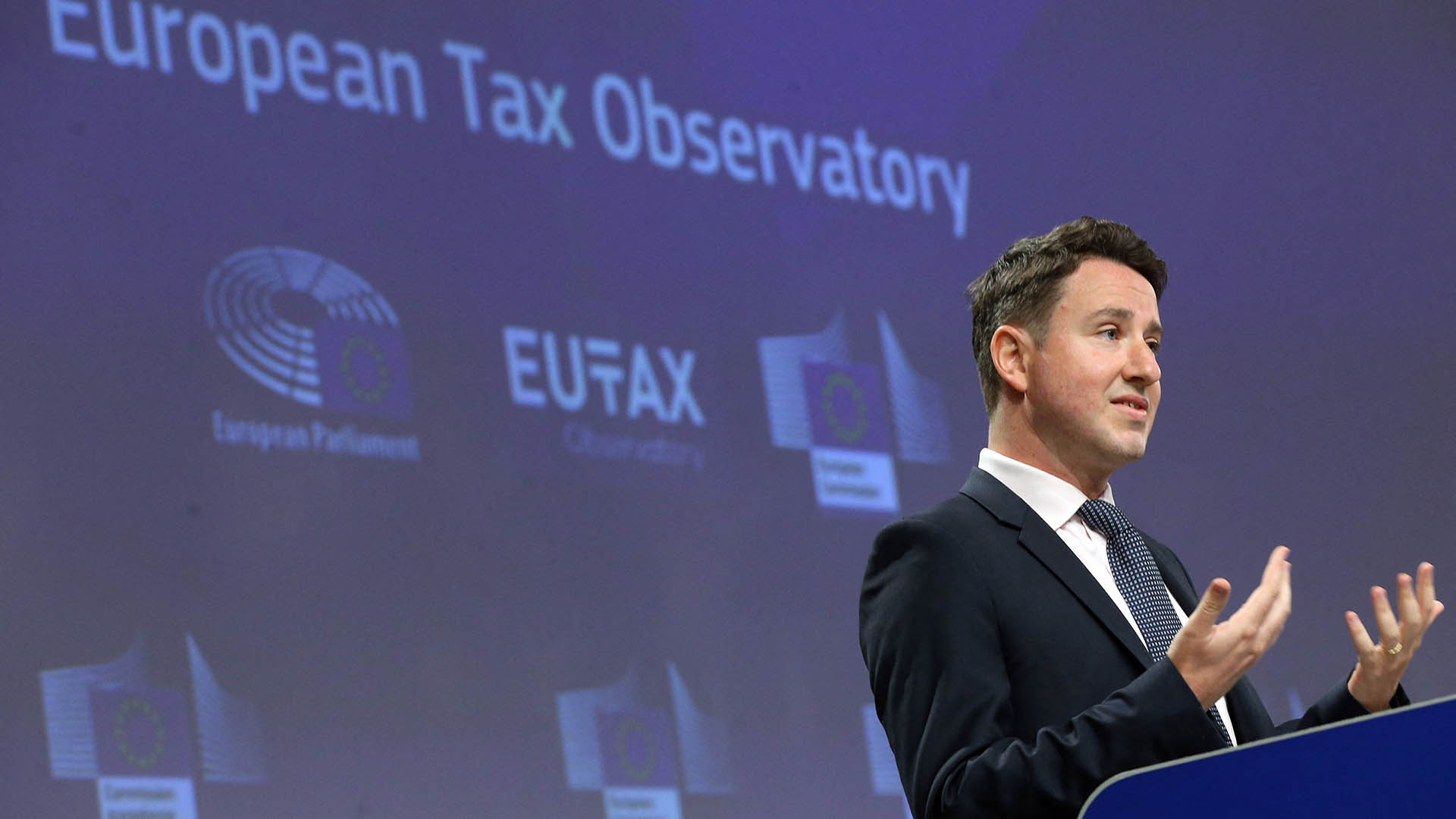 Gabriel Zucman, wearing a suit, speaks at a lecturn in front of a sign reading European Tax Observatory.