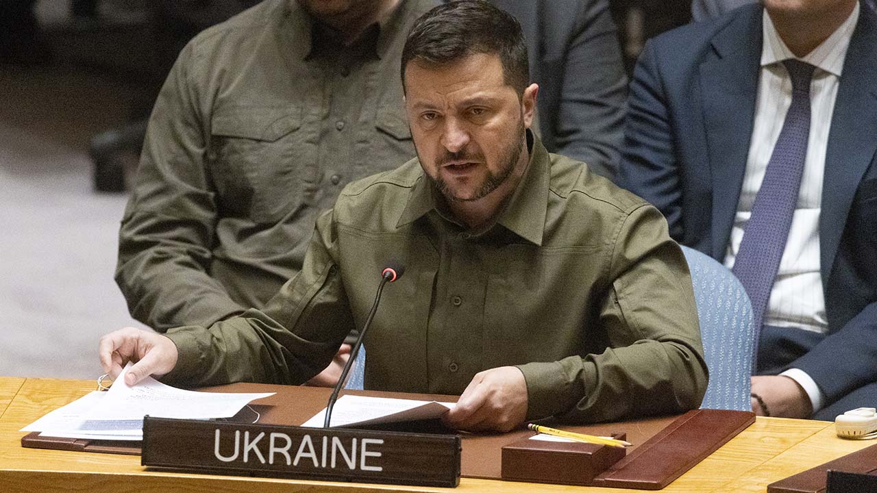 Volodomyr Zelenskyy sitting at a desk at the UN behind a nameplate that reads Ukraine.