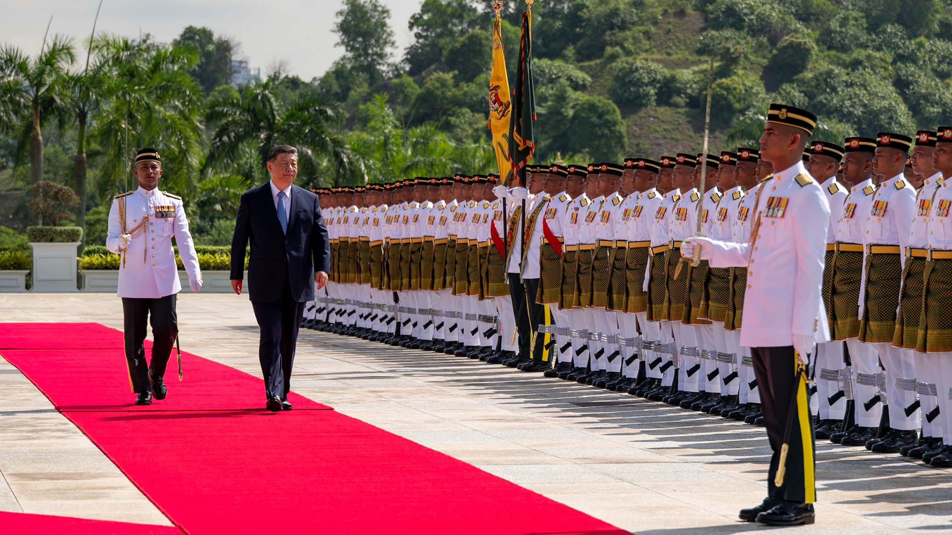 Photo of Xi Jinping walking along a red carpet in front of a troop of Malaysian soldiers in white uniforms.