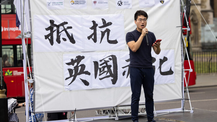 An activist dressed in black speaks in front of a sign with Chinese characters