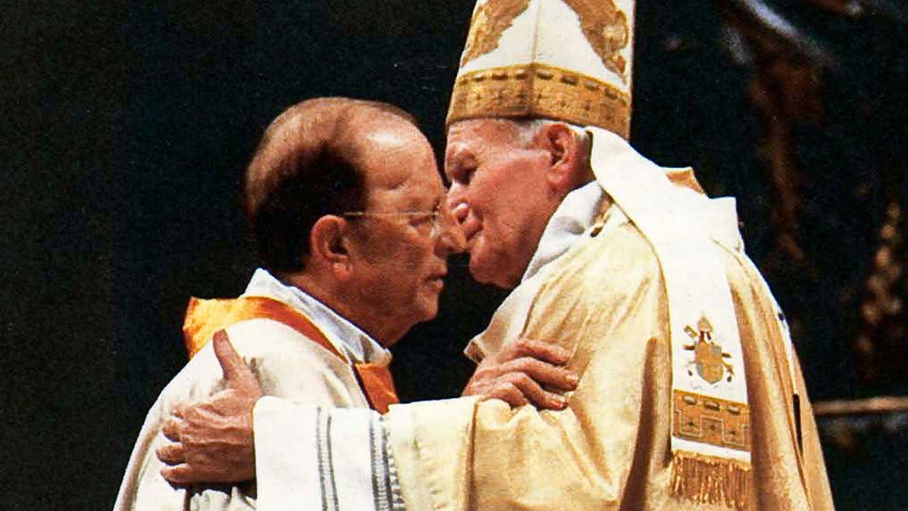 Priest Marcial Maciel, left, is embraced by Pope John Paul II, both wearing ceremonial robes against a dark backdrop.