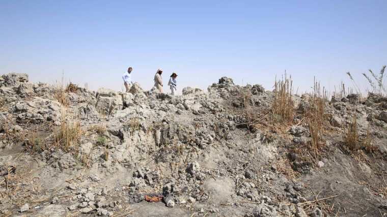 Photo of a desolate, rocky site with three people walking in the background, and remnants of clothes visible in the forgeround.