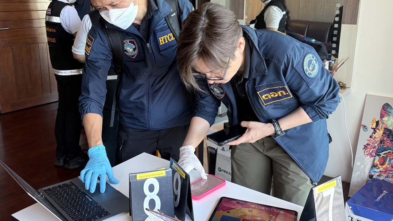 Photo of uniformed police officers inspecting laptops and mobile phones seized during a raid.