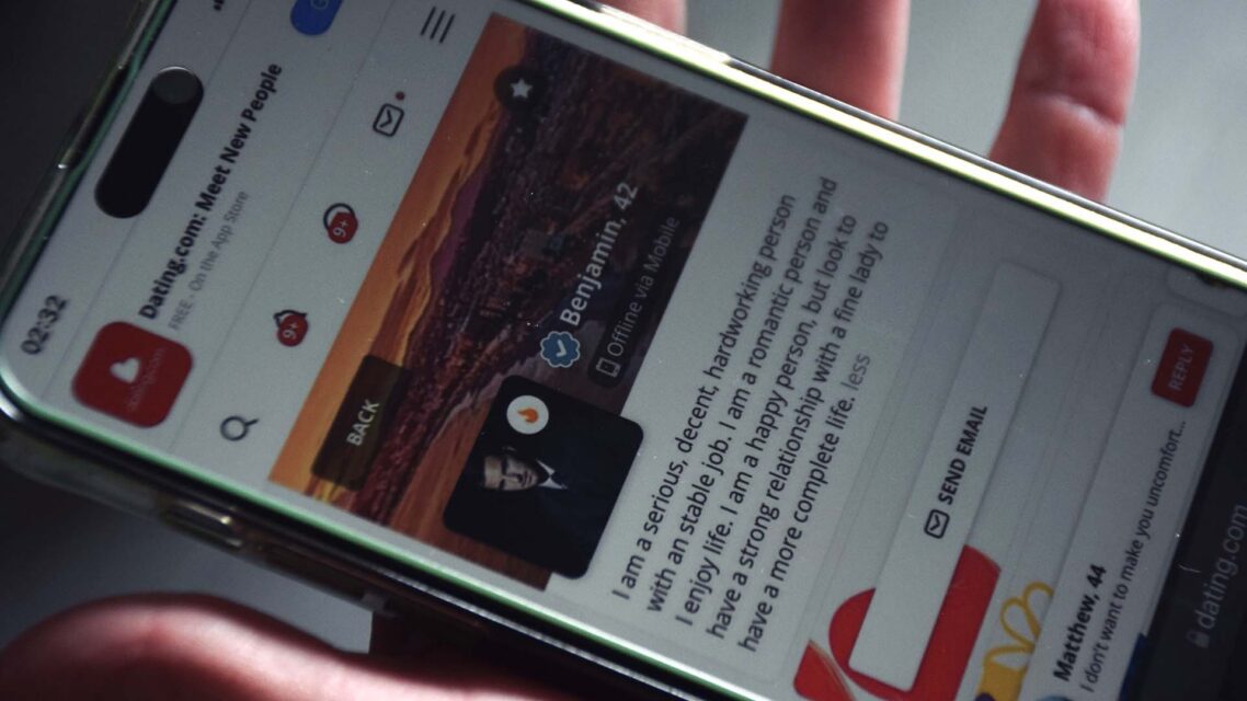 Photo of a person holding a mobile phone with messages from a dating website on the screen.