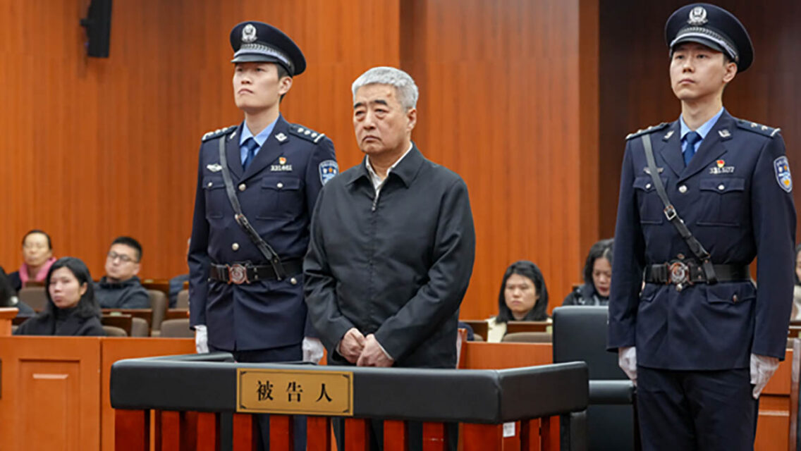 Photo of Zhang Hongli standing in a court room, flanked by two security officers.